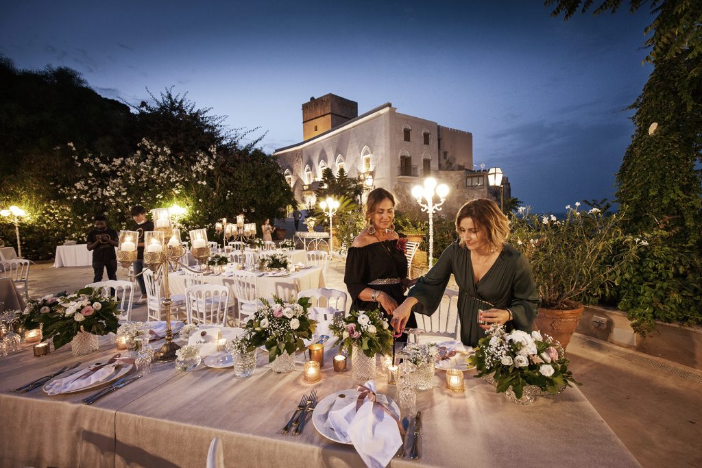 In questa foto la Wedding Planner di Palermo Antonella Candido con una sua collaboratrice controlla la mise en place di un ricevimento di nozze serale sulla terrazza del Castello di Solanto