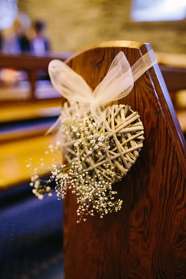 In questa foto un cuore bianco di vimini intrecciato con nebbiolina, legato con un nastro di tulle al banco di una chiesa