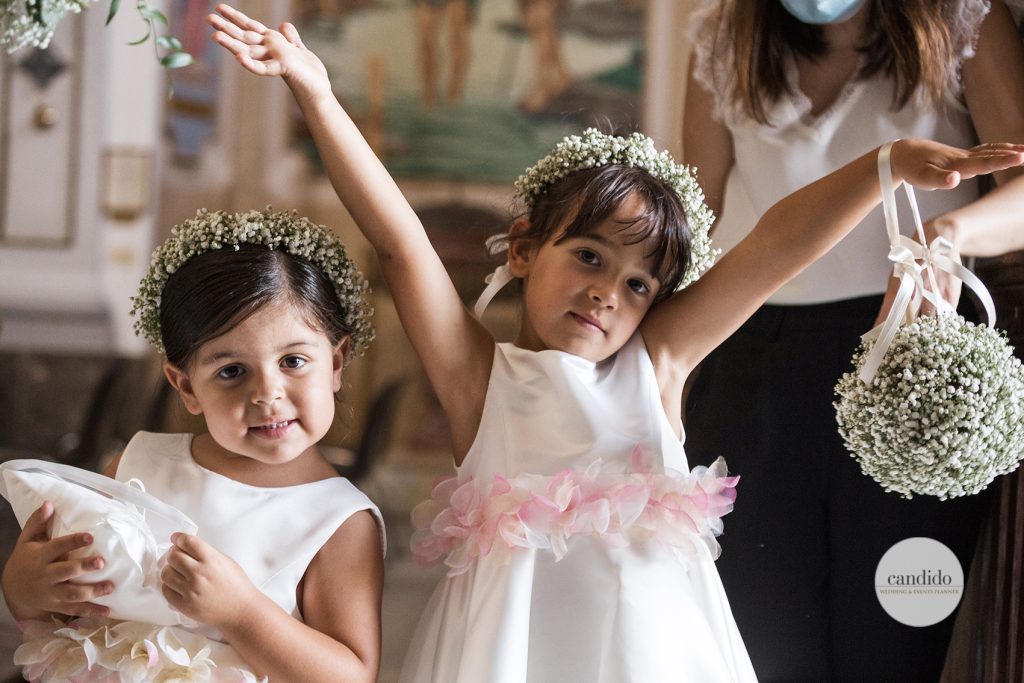 In questa foto due piccole damigelle con cerchietti e bouquet sferici di nebbiolina. I vestiti bianchi hanno una cintura di fiori di stoffa rosa