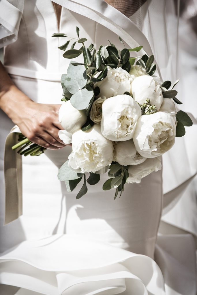 In questa foto un bouquet di peonie bianche e foglie di eucalipto stretto in mano da una sposa