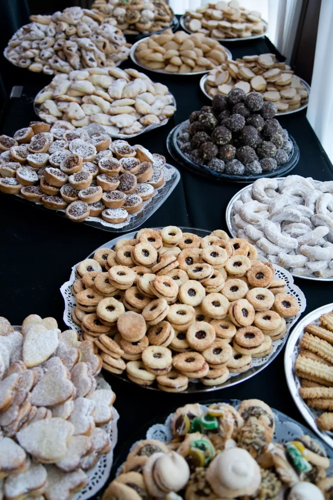 In questa foto un tavolo ripreso leggermente dall'alto con vassoi d'argento ricolmi di biscottini, dolci e dessert