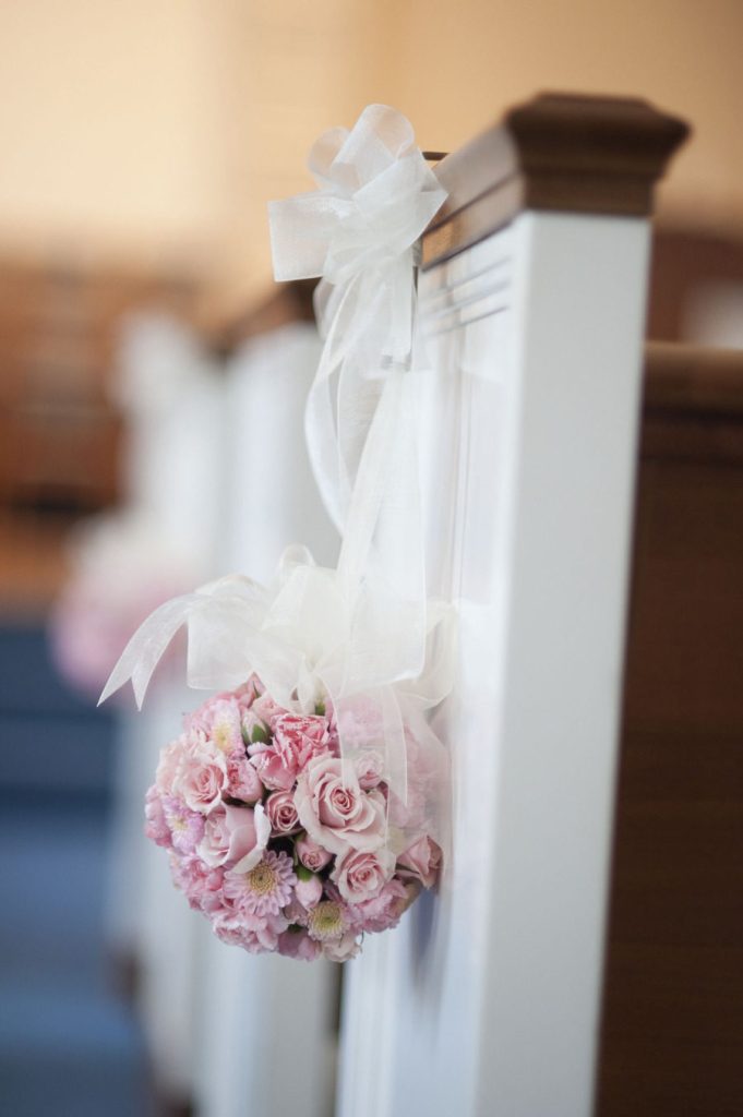 In questa foto una sfera di boccioli di rose rosa legata al banco bianco di una chiesa con un nastro largo di organza