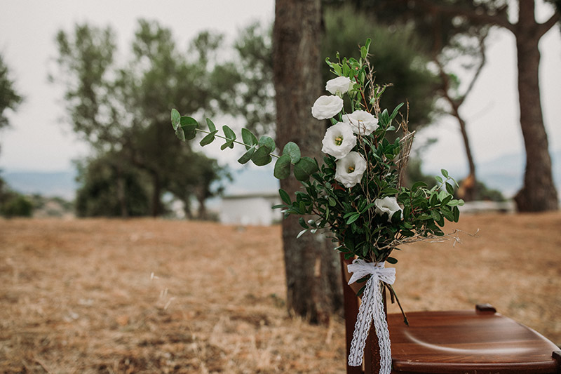 In questa foto una sedia allestita con un mazzo di fiori ranuncoli bianchi e foglie di eucalipto, nelle nozze firmate maria Rita Iai