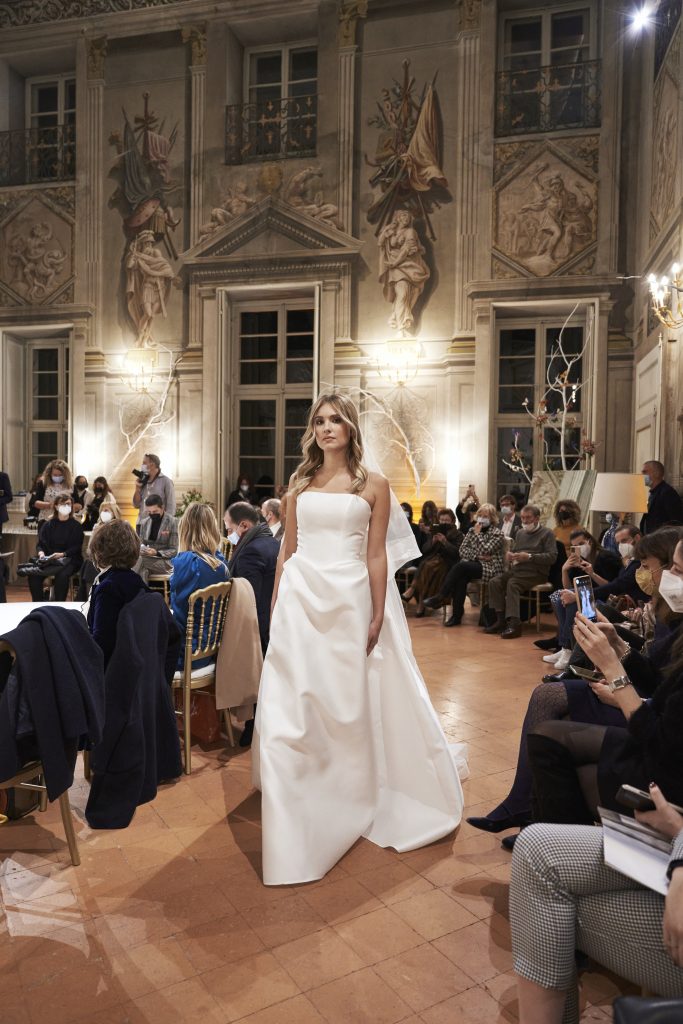 In questa foto una modella sfila indossando un abito da sposa bianco con fiocco maxi sulla schiena, firmato da Maria Pia Creazioni per Revenge Atelier 2022