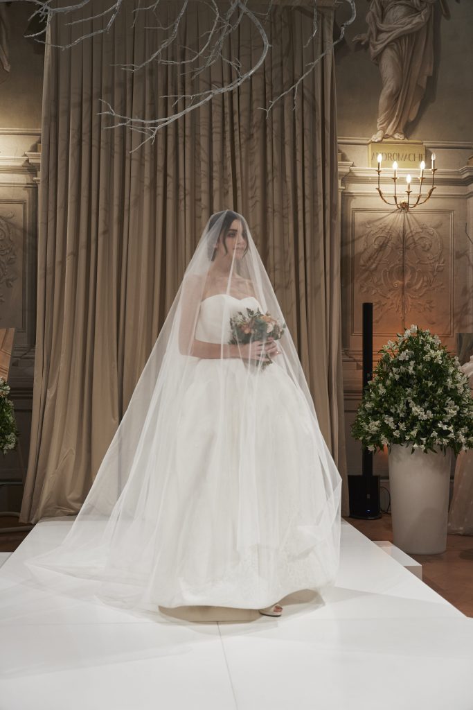 In questa foto una modella in passerella con addosso un abito da sposa con scollo a cuore della capsule collection Revenge Atelier