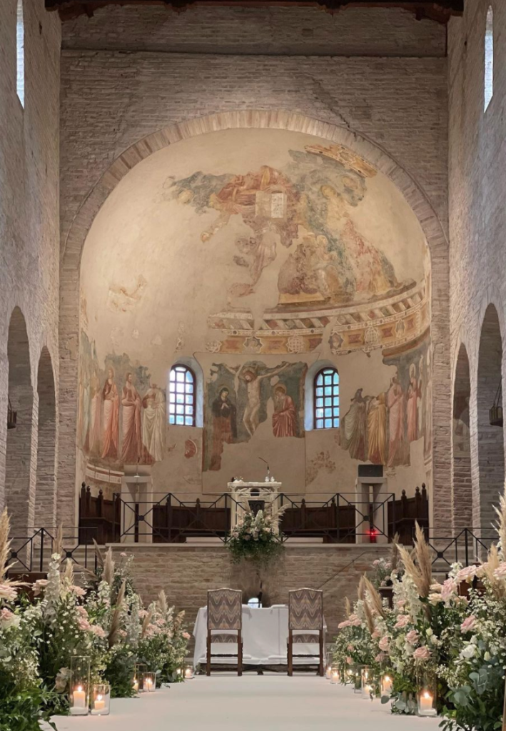 In questa foto una chiesa semplice con mattoni chiari decorata per un matrimonio con composizioni di rose rosa, bianche, nebbiolina e pampas e candele accese. La stessa composizione è presente anche all'altare