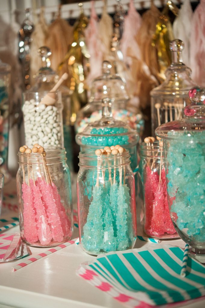 In questa foto un tavolo per la confettata con confettini bianchi, caramelle rosa e verde tiffany contenute in bocce di vetro e tovagliolini a righe nei colori abbinati