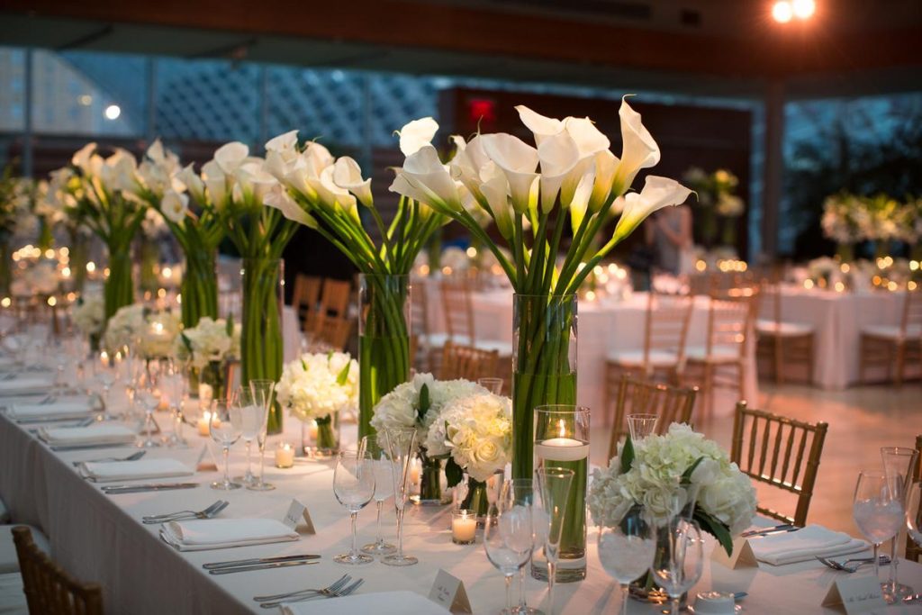 In questa foto un tavolo rettangolare per matrimonio inquadrato in obliquo a sinistra decorato con composizioni di calle e roselline bianche e candele