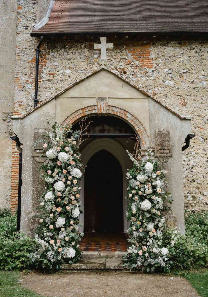 In questa foto l'esterno della chiesetta di campagna di mattoni decorato sui lati con grandi fiori bianchi, roselline rosa, foglie, nebbiolina e rametti