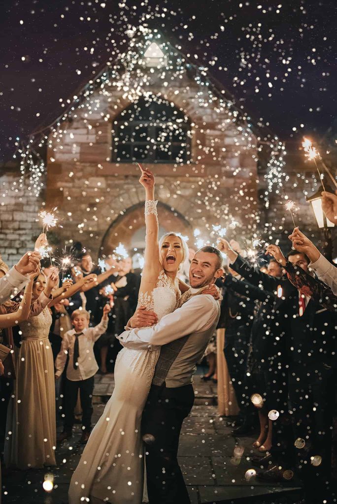 In questa foto uno sposo tiene in braccio la spoa che urla felice mentre attorno a loro gli ospiti agitano le scintille accese 