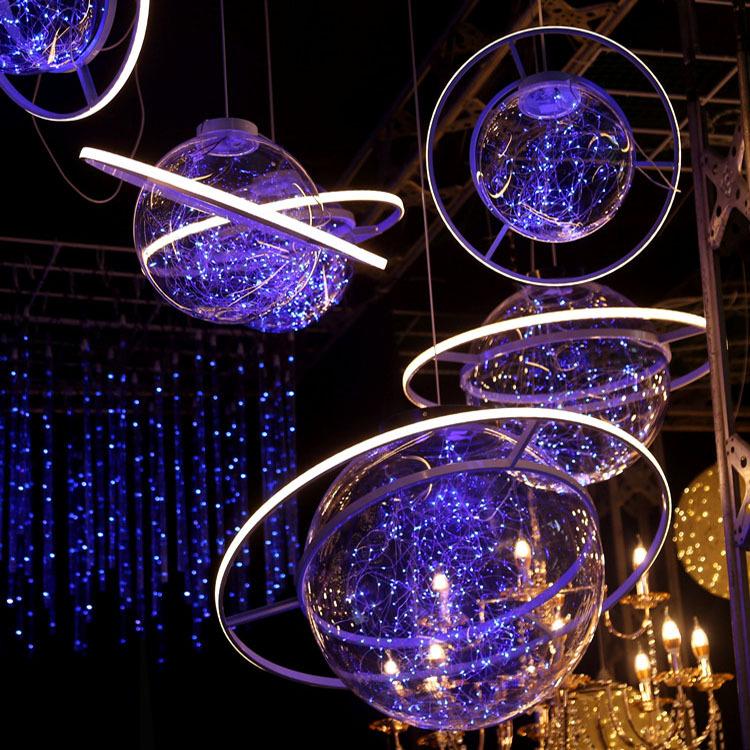 In questa foto sfere di luci blu a forma di pianeti decorato la sala di un ricevimento accanto ad alcuni lampadari