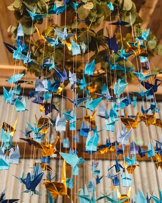In questa foto allestimenti matrimonio composti da fili con gru origami colore azzurro, blu, e oro che pendono dal soffitto 