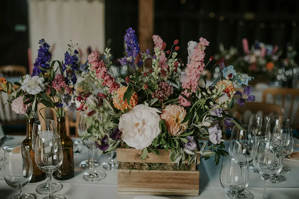 In questa foto un centrotavola con fiori di campo viola, rosa e bianchi in una cassetta di legno 