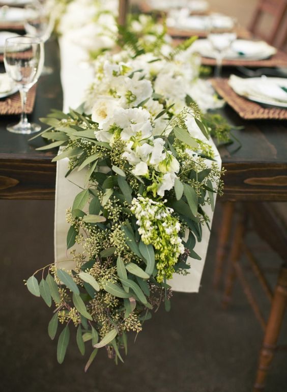 Runner floreale di Lisianthus bianchi e rami di eucalipto verdi, adagiato su un runner di tessuto bianco. 