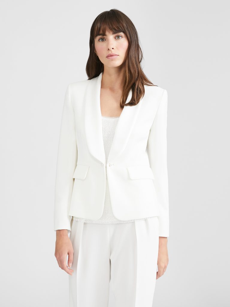 In questa foto una modella indossa un tailleur con pantaloni di colore bianco del brand Max Mara. Modello smoking. La giacca, blazer sagomato con un bottone. Reverse su tinta. 