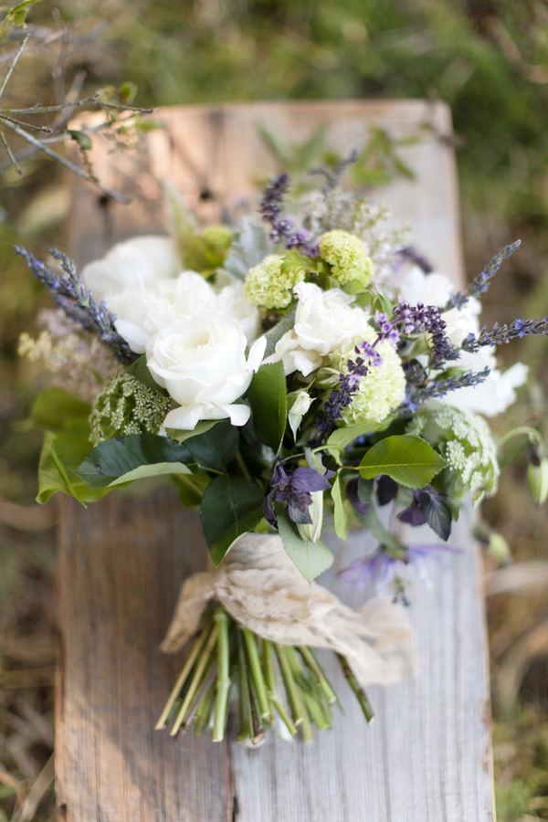 Un bouquet di rose bianche e foglie di eucalipto verdi e rami di lavanda. Il bouquet è legato con un nastro di juta. 