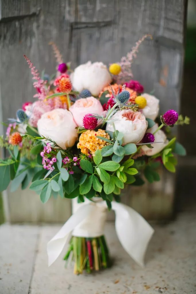 Un bouquet di rose inglesi rosa, ortensie gialle e fiori di campo viola e fucsia, lavanda. Il mazzo è legato con un nastro di seta bianco. 