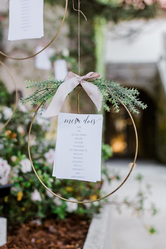 In questa foto un tableau mariage a tema natalizio realizzato con piccoli cerchi dorati decorati con aghi di pino e nastri rosa a cui sono appese le card con gli elenchi degli ospiti