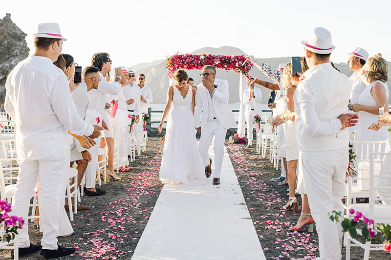 L'uscita degli sposi dopo la celebrazione del matrimonio civile. Tra gli ospiti, tutti vestiti di bianco. Lungo il tappeto bianco, petali di buoganvillea e rose fucsia