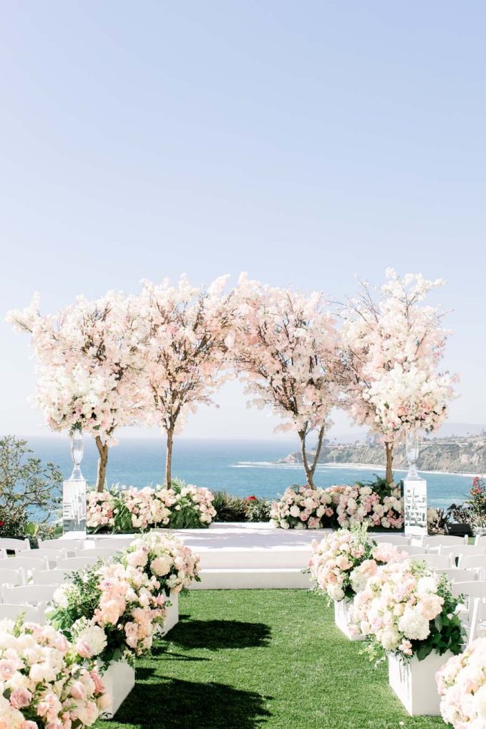 In questa foto l'allestimento per un matrimonio civile sul mare. Il prato è decorato con fiori bianchi e rosa mentre lo spazio dedicato al rito è circondato di alberi di ciliegio