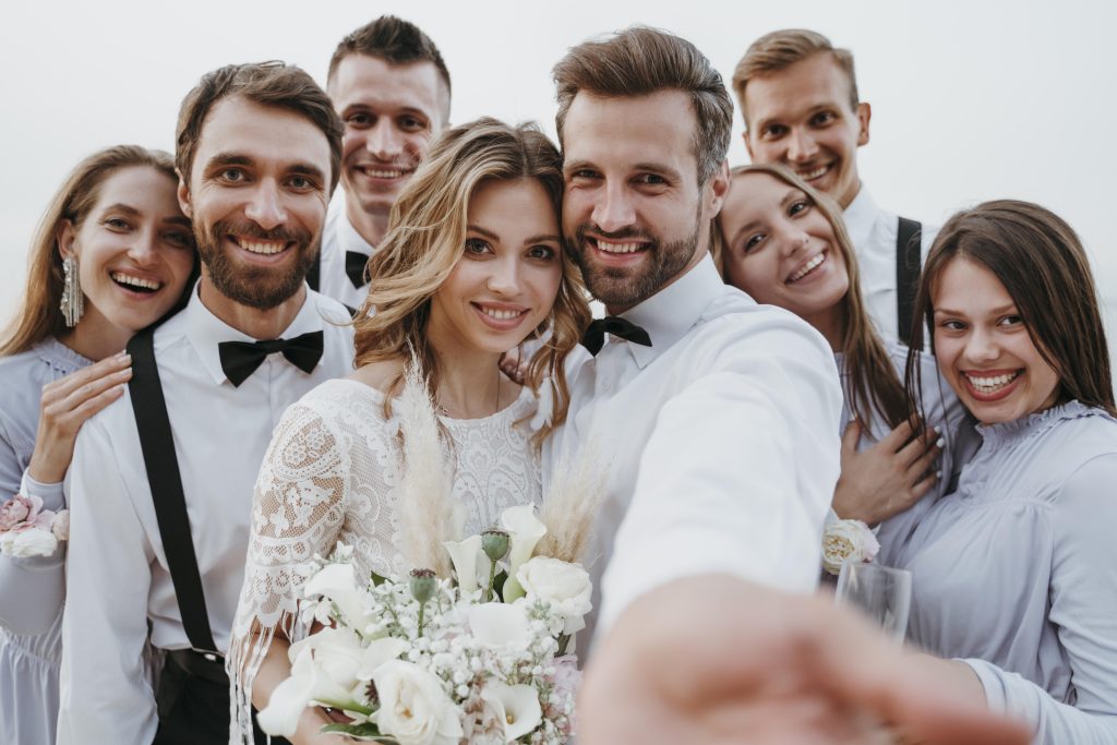 In questa foto due sposi si scattano un selfie circondati dai loro testimoni di nozze