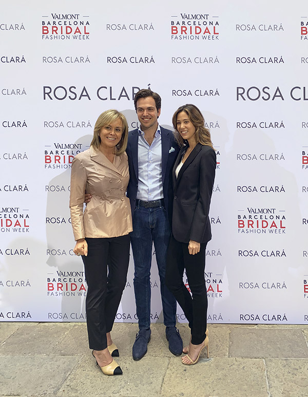 Da sinistra, Rosa Clarà, Daniel Clarà e Anne-Marie Colling con alle spalle un cartellone del marchio spagnolo Rosa Clarà esposto alla Barcelona Bridal Fashion Week