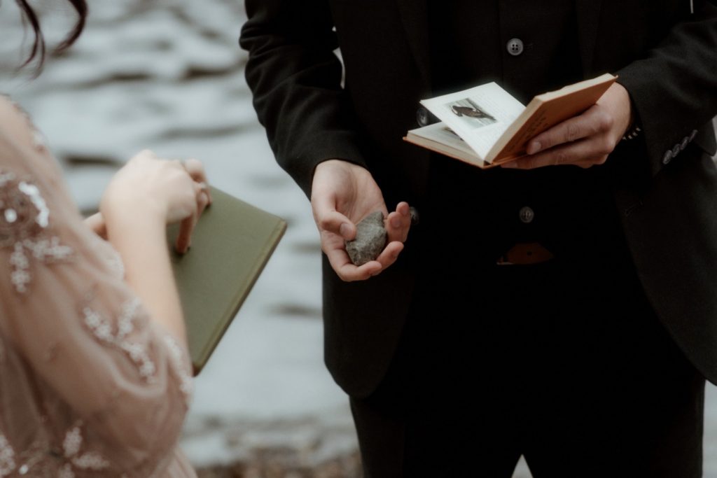 In questa foto uno dei riti simbolici per matrimonio antichi: il rituale della pietra del giuramento. Lo sposo è ripreso frontalmente mentre tiene nella mano destra una pietra e nella mano sinistra un piccolo libretto. Di fronte a lui la sposa ripresa di spalle di cui è mostrato solo il gomito destro sta per aprire il suo libretto