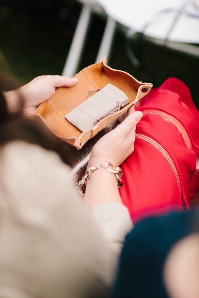 In questa foto un'invitata ripresa di spalle tiene in mano uno svuota tasche di pelle con un sacchetto di pelle contenente le fedi nuziale durante la celebrazione del rito simbolico per matrimonio del calore degli anelli