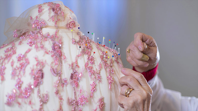 Una sarta dell'atelier Sofia Provera Sposa cuce a mano un ricam rosa su un abito da sposa