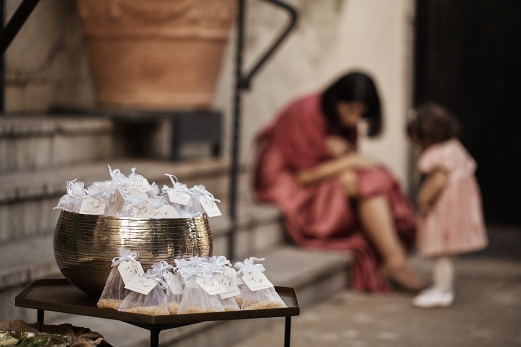 In questa foto in primo piano una coppa d'argento con sacchetti di riso. Sullo sfondo una donna vestita di rosa seduta con una bambina