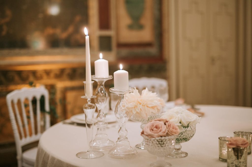 In questa foto una mise en place romantica con vasi di cristallo e portacandele trasparenti con fiori rosa e bianchi