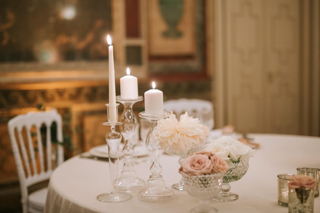 In questa foto una mise en place romantica con vasi di cristallo e portacandele trasparenti con fiori rosa e bianchi