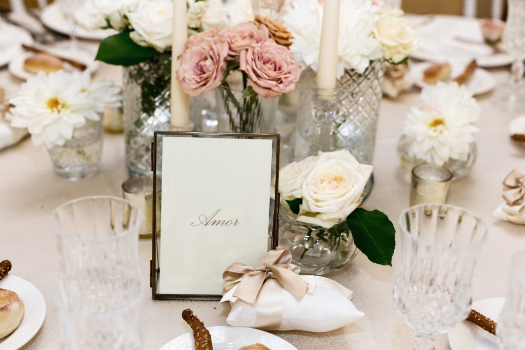 In questa foto il dettaglio di una mise en place romantica. In evidenza il nome del tavolo "Amor" e un sacchetto di confetti bianco con nastro colore oro