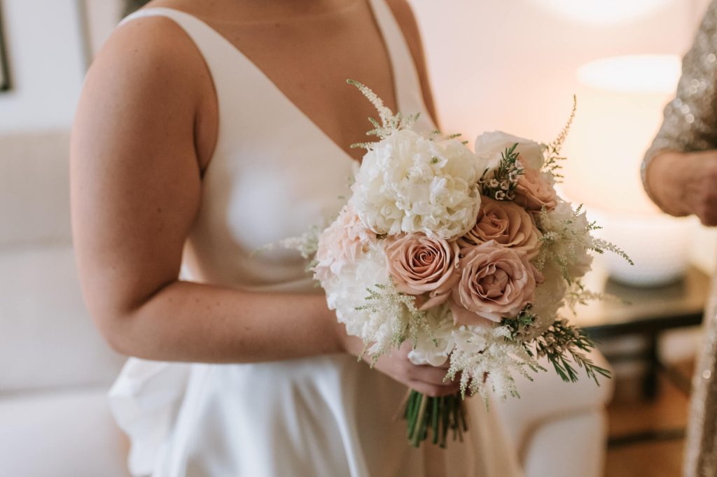 In questa foto il bouquet rotondo di una sposa con rose rosa e fiori bianchi