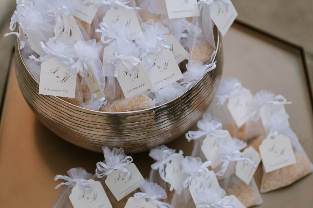 In questa foto una coppa in argento con sacchetti d'organza bianchi contenenti riso e fermati da un nastro bianco e un tag con le iniziali degli sposi