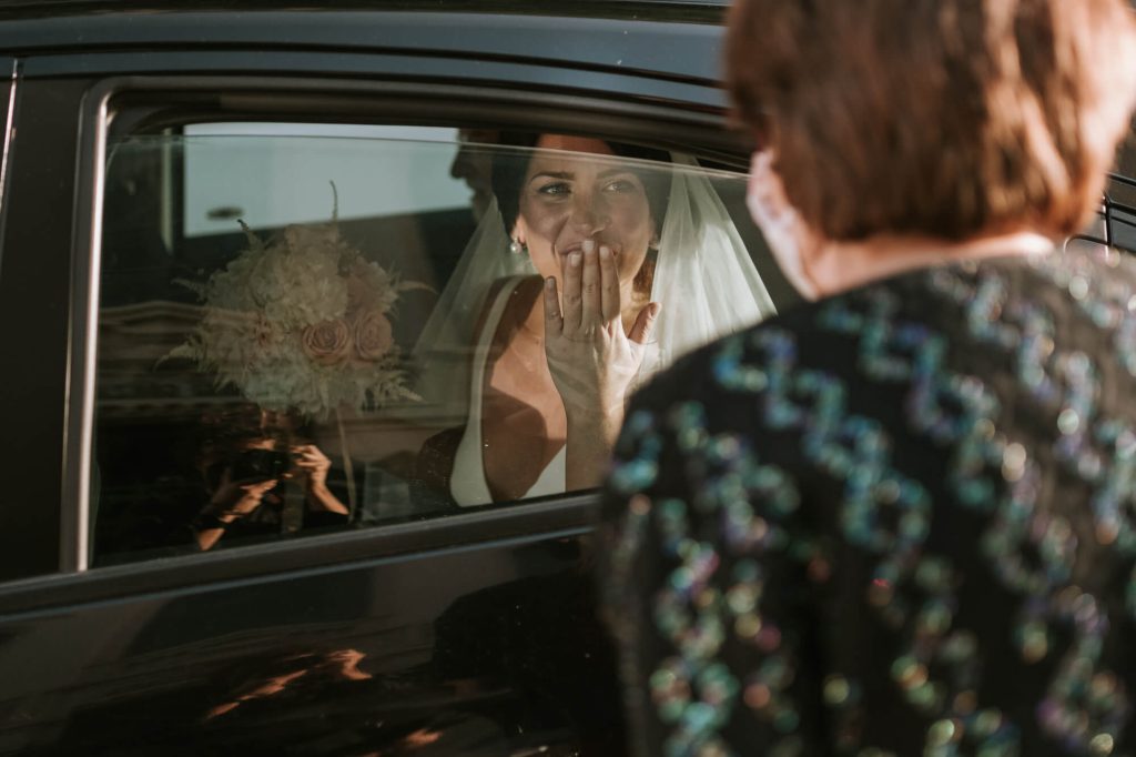 In questa foto una sposa manda un bacio alla mamma dalla sua auto