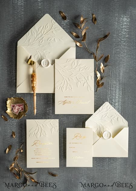 Nella foto, inviti per matrimonio eleganti con invito e busta avorio decorati con la tecnica dell'embossing, font dorato e sigillo di ceralacca bianco perlato 