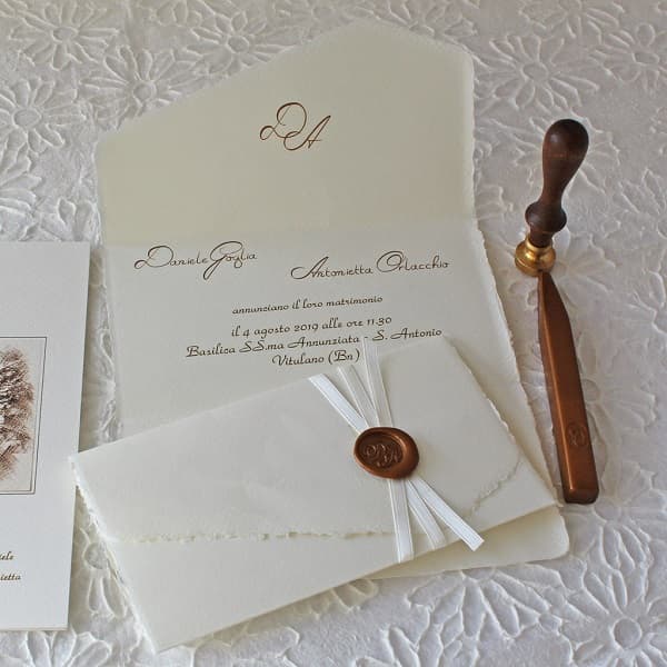 Nell'immagine, partecipazioni eleganti in carta d'Amalfi richiuse con nastrino di raso bianco e sigillo di ceralacca color rame