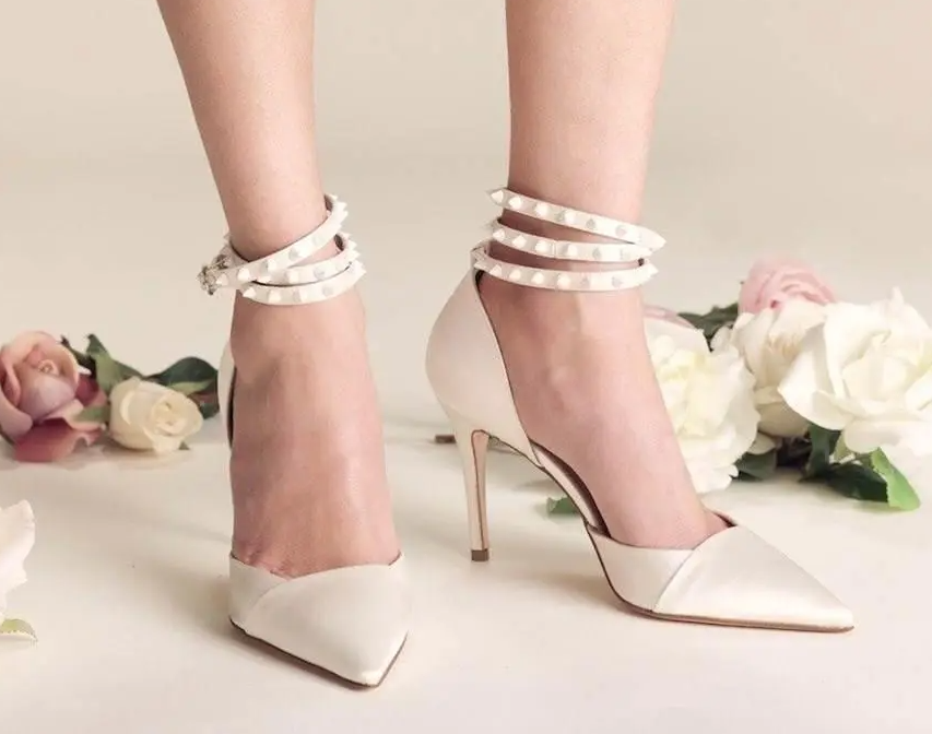 In questa foto i piedi di una modella che indossa un paio di scarpe décolleté del brand Serrese: sulla caviglia dei lacci borchiati. Il modello fa parte della collezione scarpe sposa 2022 