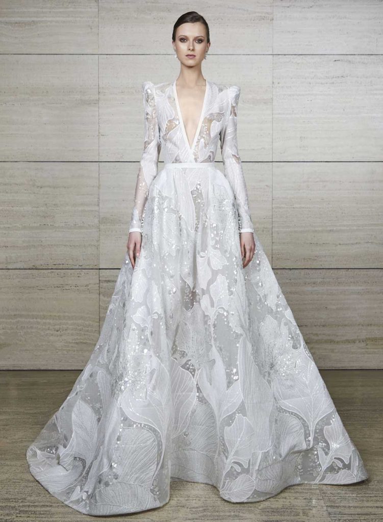 In questa foto una modella indossa un abito da sposa con le maniche 2022 della collezione Elie Saab. L'abito svasato, con maniche lunghe e spalline militari, è interamente ricoperto da un pattern floreale.
