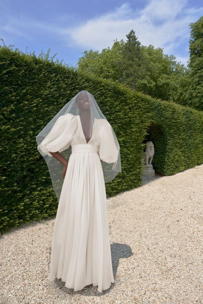 In questa foto una modella indossa un abito da sposa con le maniche 2022 della collezione Giambattista Valli. Le maniche sono ampie baloon e il vestito cade scivolato.