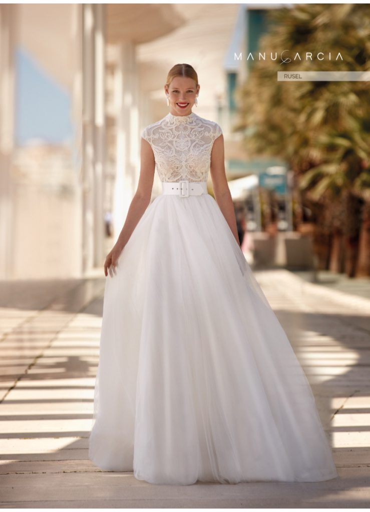 In questa foto una modella indossa un abito da sposa con le maniche 2022 della collezione Manu Garcia. L'abito è ampio con un corsetto con maniche corte con motivo simmetrico.