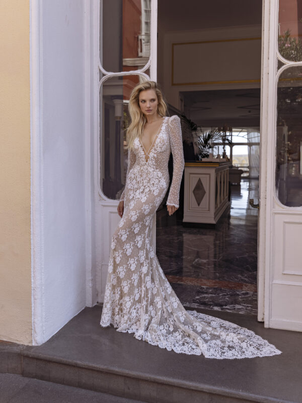 In questa foto una modella indossa un abito da sposa con le maniche 2022 della collezione Michela Ferriero. L'abito  è a sirena di pizzo, con maniche di pizzo e un profondo scollo a V.