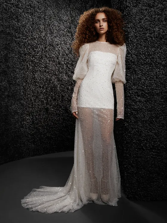 In questa foto una modella indossa un abito da sposa con le maniche 2022 della collezione Vera Wang. L'abito ha un doppio strato con una trasparenza ricoperta di paillettes e delle maniche a sbuffo.
