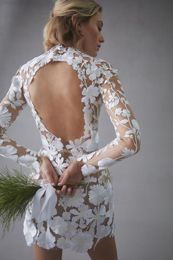 In questa foto una modella indossa un abito da sposa schiena scollata 2022 della collezione Oscar de la Renta con scollo profondo e maniche lunghe di pizzo.