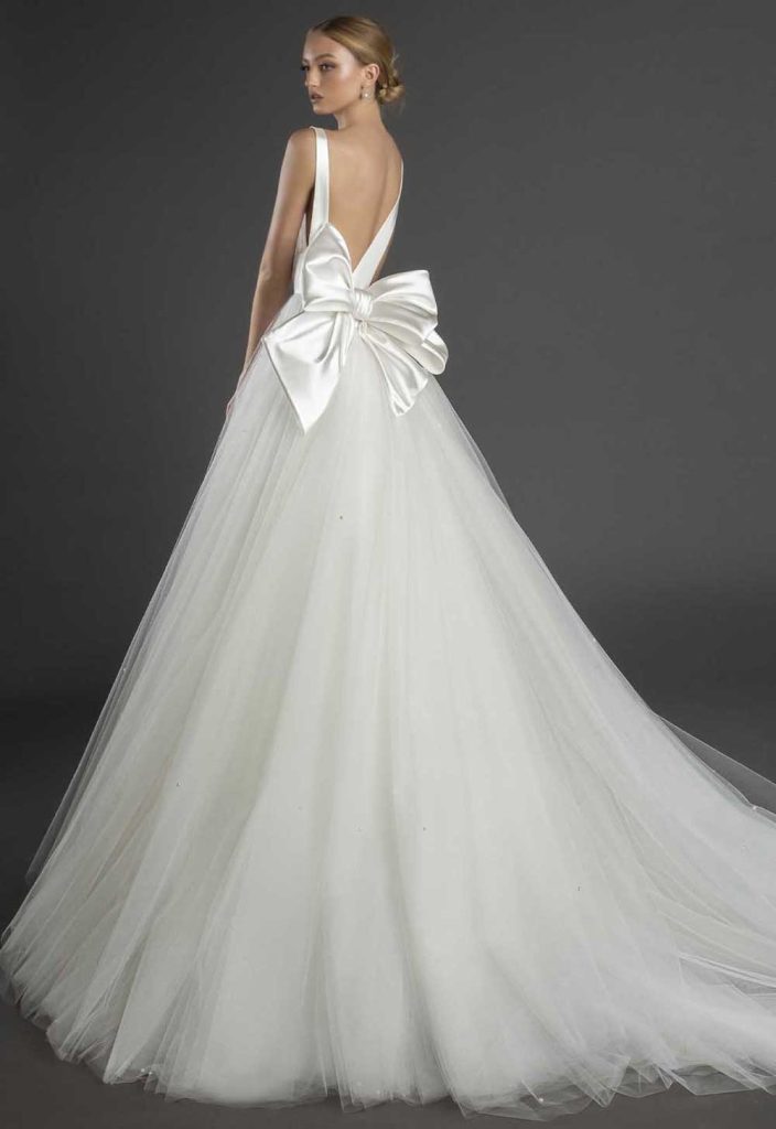 In questa foto una modella indossa un abito da sposa schiena scollata 2022 della collezione Pnina Tornai con scollo profondo e maxi fiocco.