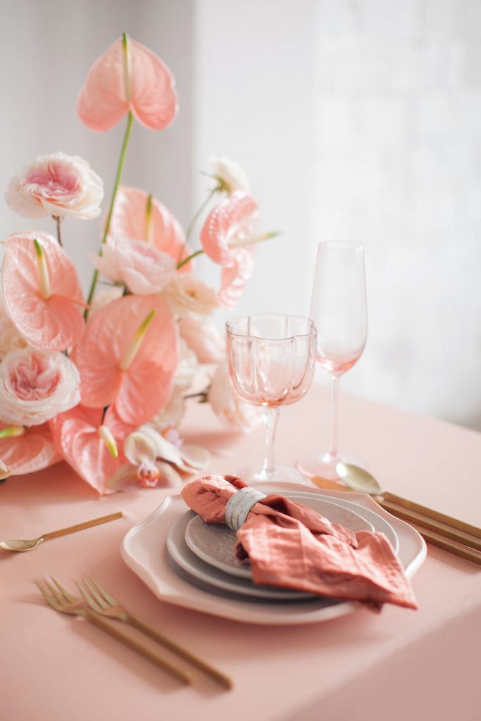 In questa foto una tavola in stile elegante con tovagliato, bicchieri e centrotavola di fiori matrimonio rosa e posate colore oro. I tipi di fiori scelti sono le rose inglesi e l'anthurium