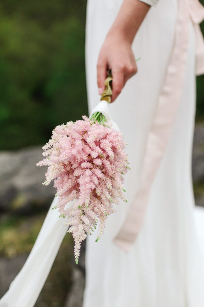 In questa la mano di una sposa che tiene un piccolo bouquet di astilbe rosa