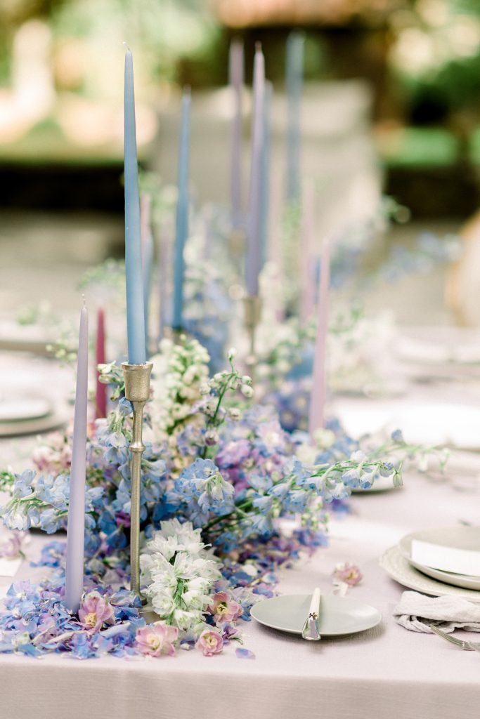 In questa foto il dettaglio di un runner con fiori matrimonio blu, bianchi e viola e candele abbinate in portacandele colore argento su un tavolo imperiale 