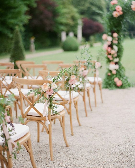 In questa foto il dettaglio di sedie cross disposte per un matrimonio civile e decorate con un mazzolino di 3 rose in 3 gradazioni di rosa con foglie di ulivo